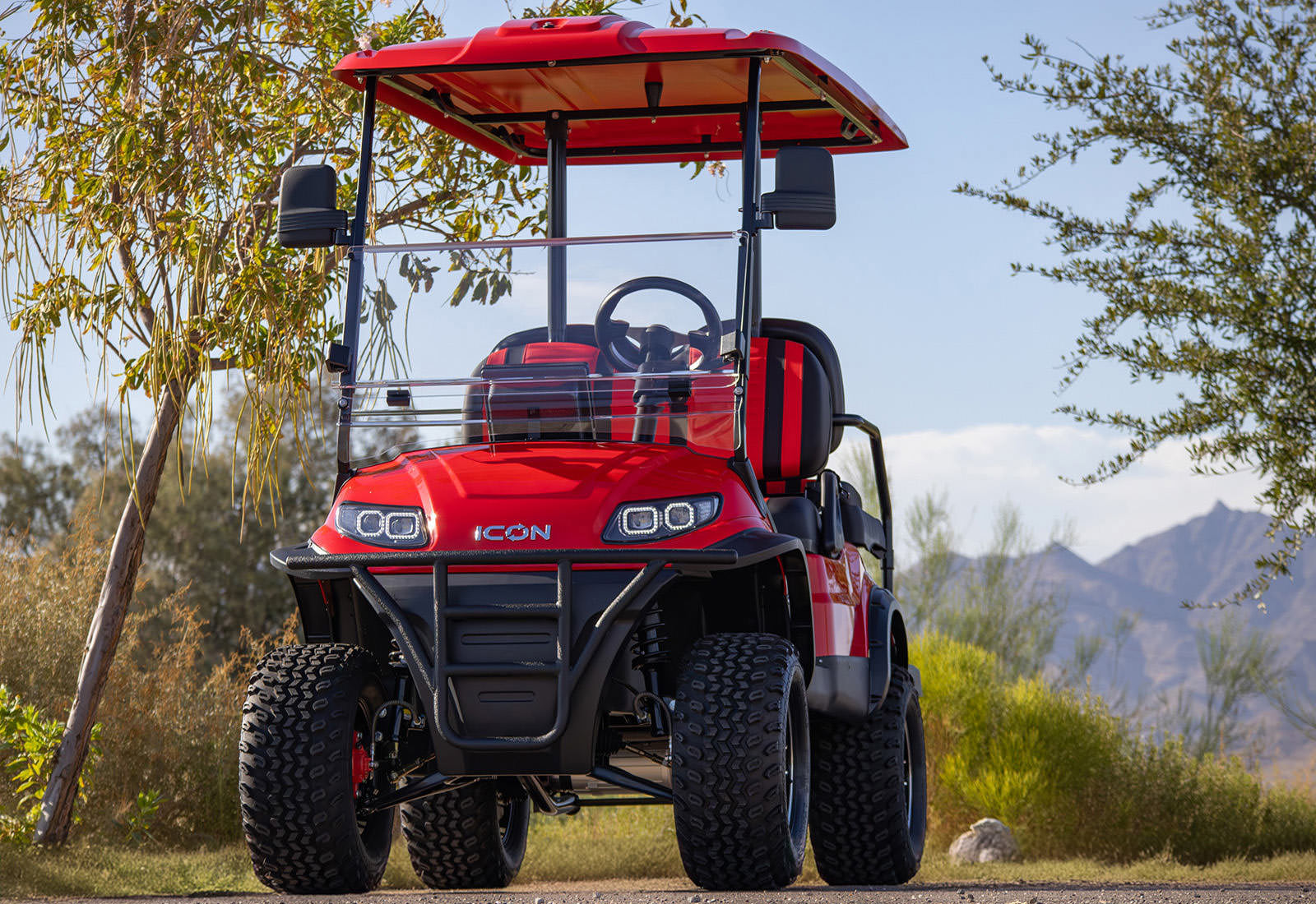 Red icon off-road vehicle on a scenic path with trees and mountains in the background