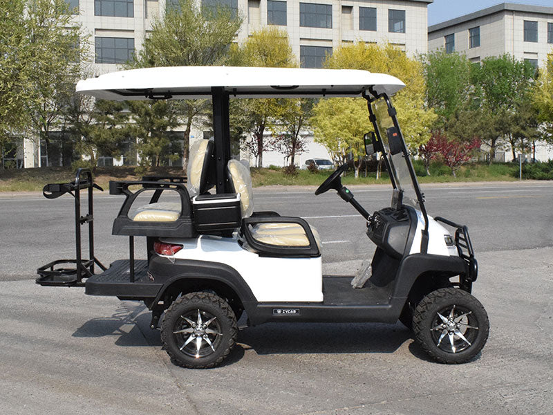 ocean cartz side profile view of a white four-seater golf cart with a white roof, parked on an asphalt street. This lifted off-road electric vehicle features tan or cream-colored seats, a rear cargo area with a golf bag holder, and a front brush guard. The all-terrain golf cart is equipped with large, knobby off-road tires on custom silver and black wheels.