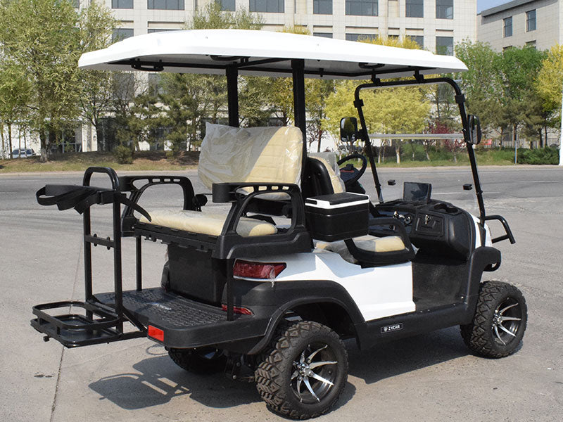 ocean cartz rear three-quarter view of a white six-seater golf cart with a white roof, showing the rear flip seat folded down to a cargo bed. This lifted off-road electric vehicle features tan or cream-colored seats, a cooler box, and a golf bag holder rack attached to the back. The all-terrain golf cart is equipped with large, knobby off-road tires on custom black and silver wheels.