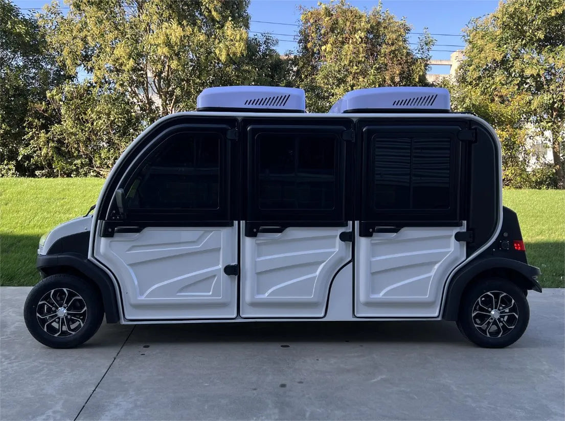 White electric vehicle with open doors on a concrete surface, surrounded by greenery.