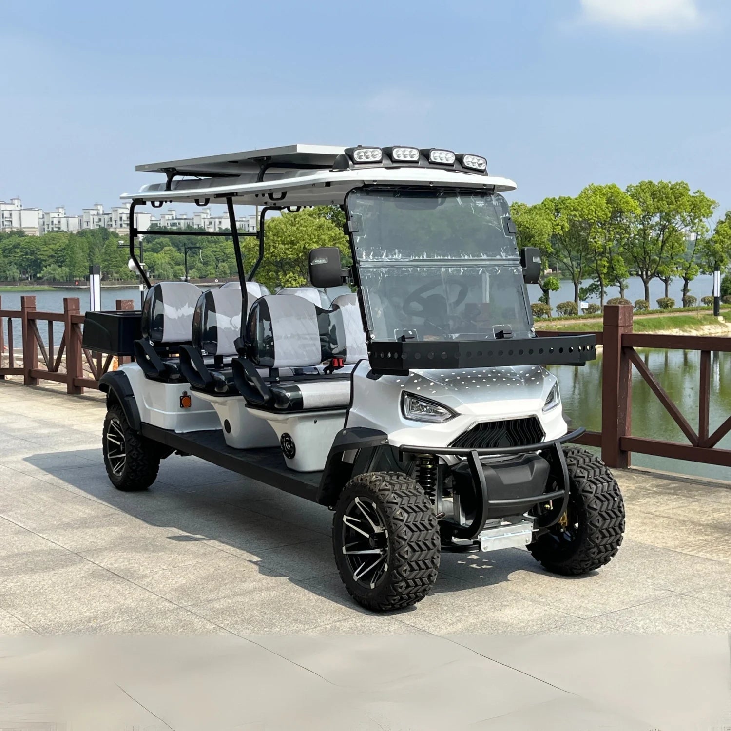 White golf cart with black accents parked by a lake with greenery and buildings in the background.