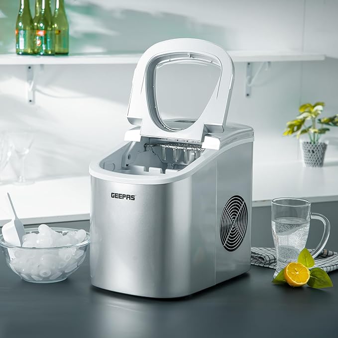 Silver GEEPAS ice maker on a kitchen counter with a glass of water and lemon.