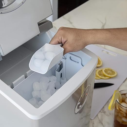 Hand using a scoop to take ice from a portable ice maker on a kitchen counter.