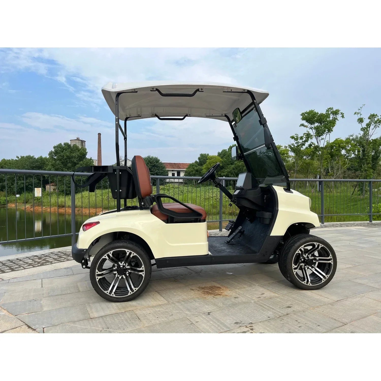 Side view of cream-colored golf cart with brown seats and large alloy wheels on stone pavement.