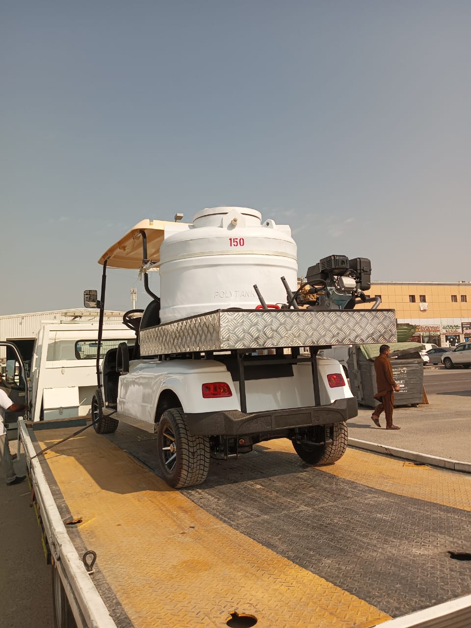 A white utility golf cart carries a large water tank on its bed.