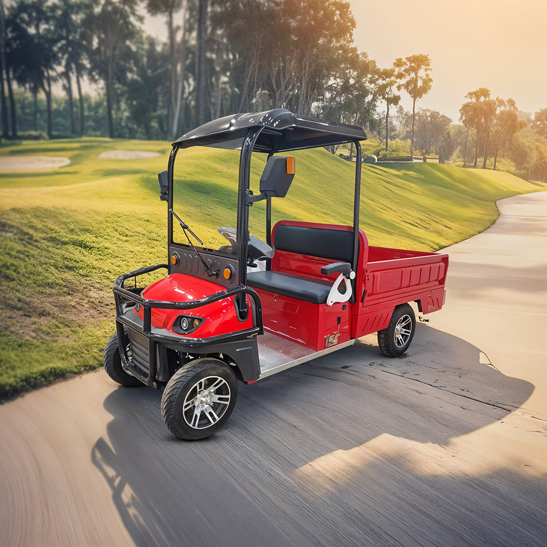 ocean cartz three-quarter front view of a red utility electric vehicle with a flatbed and a black roof, driving on a paved path. This two-seater work cart features black seats, a black front brush guard, and custom silver alloy wheels. The electric vehicle is designed for resort or commercial use and is pictured on a path winding through a sunny, lush green golf course or park.