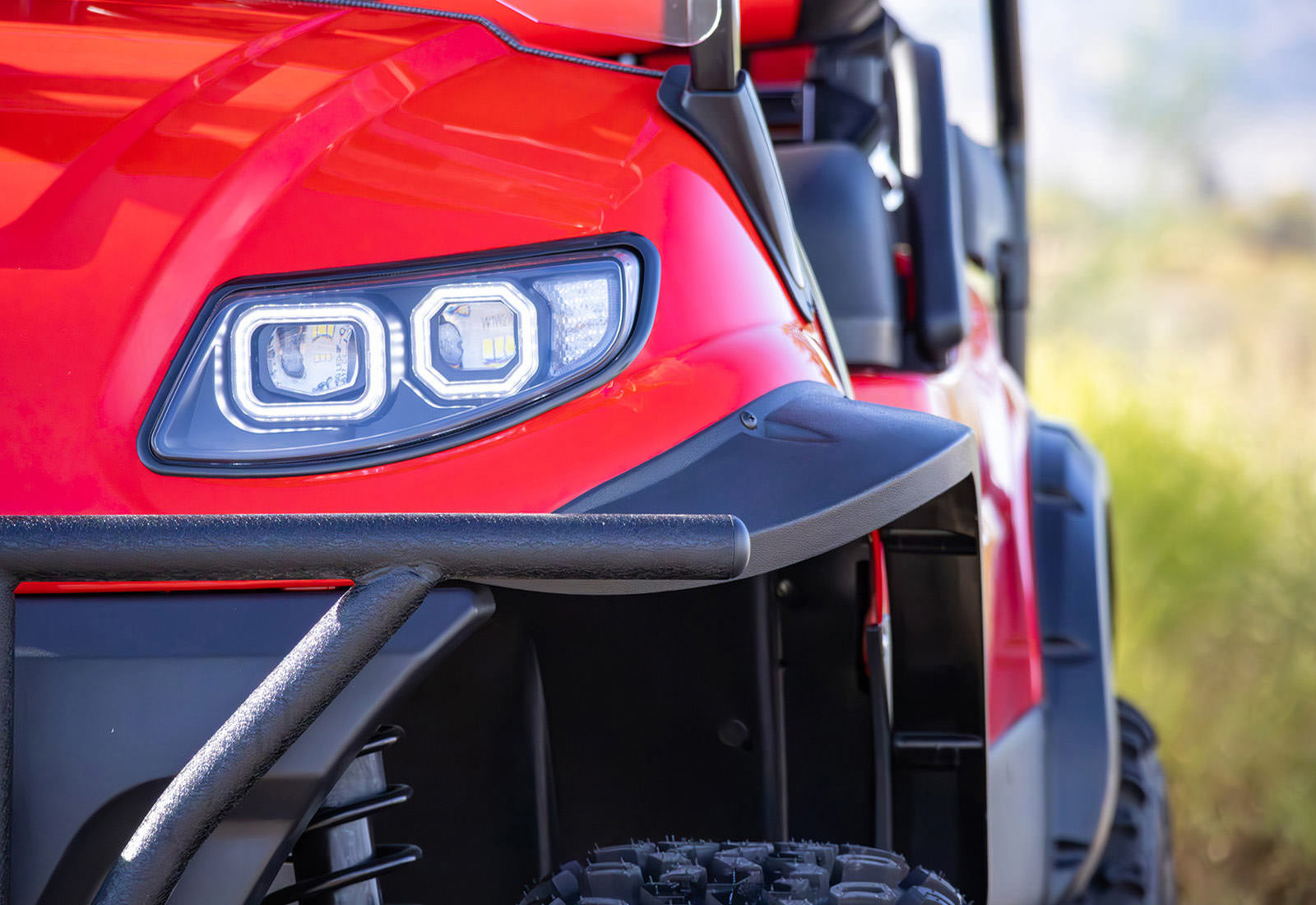 Close-up of a red off-road vehicle's headlight with a blurred natural background