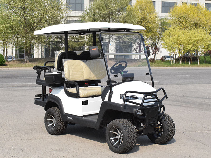 ocean cartz three-quarter front view of a white four-seater golf cart with a white roof, parked on an asphalt street. This lifted off-road electric vehicle features a black front brush guard, tan or cream-colored seats covered in plastic, and a rear cargo area with cup holders. The all-terrain golf cart is equipped with large, knobby off-road tires on custom silver and black wheels.