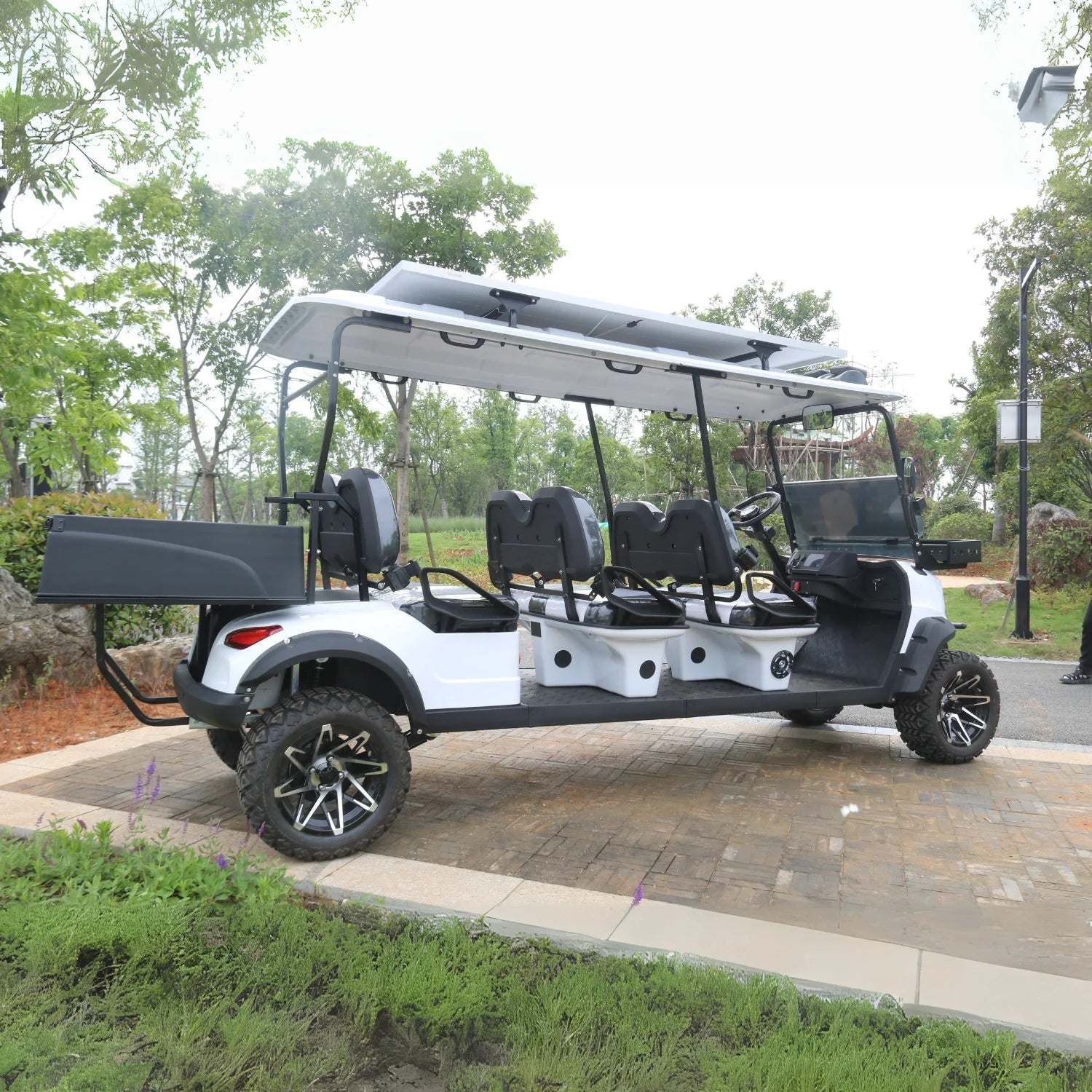 White and black golf cart with open roof on a paved path in a park-like setting.